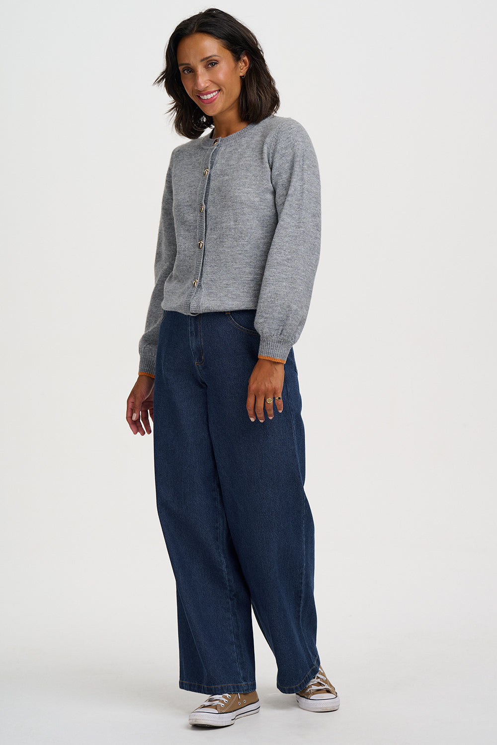 A woman modeling a light gray long-sleeve button-front cardigan and dark blue wide-leg jeans against a plain light gray studio background.