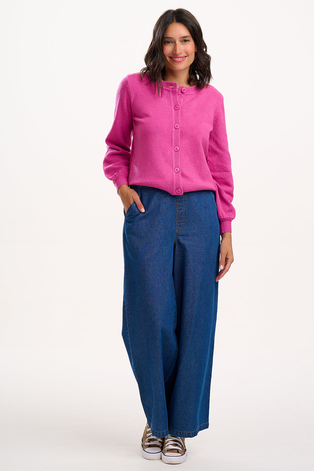 Sugarhill Brighton model  wearing a pink sweater and blue pants on a white background