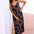 A model wearing a midi sundress with a retro geometric pattern in black, red, and blue, standing by a beachside.