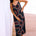 A model wearing a midi sundress with a retro geometric pattern in black, red, and blue, standing by a beachside.
