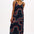 A model wearing a midi-length sundress with a black base and multicolored geometric patterns, featuring adjustable spaghetti straps.