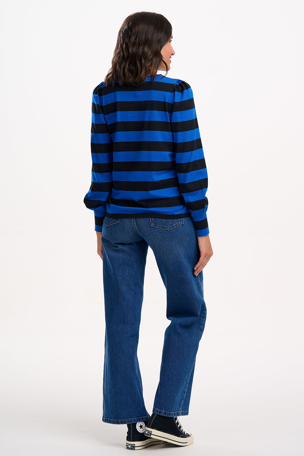 Person wearing a blue and black striped sweater and blue jeans on a white background