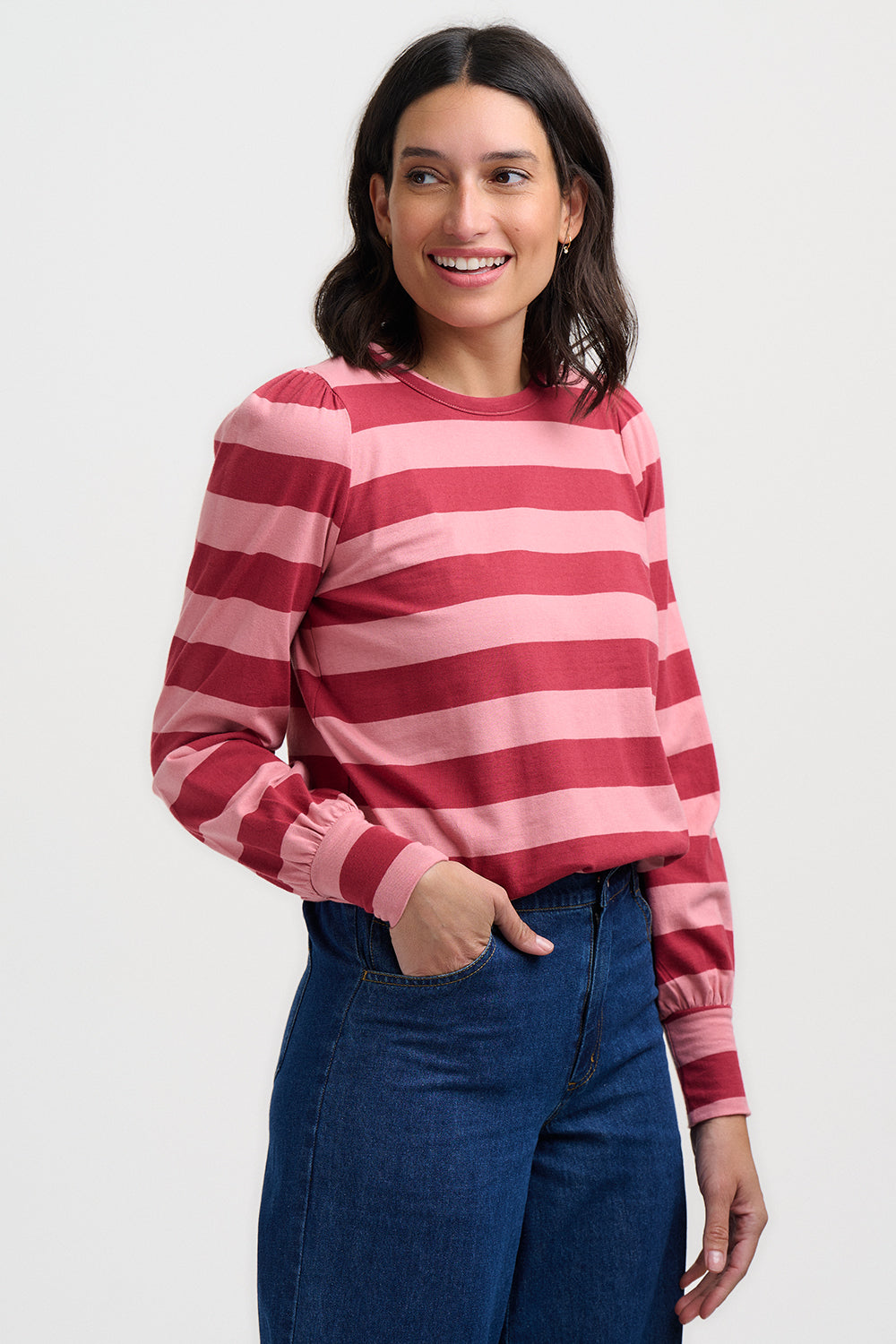 Woman wearing a red and pink striped sweater with blue jeans on a white background