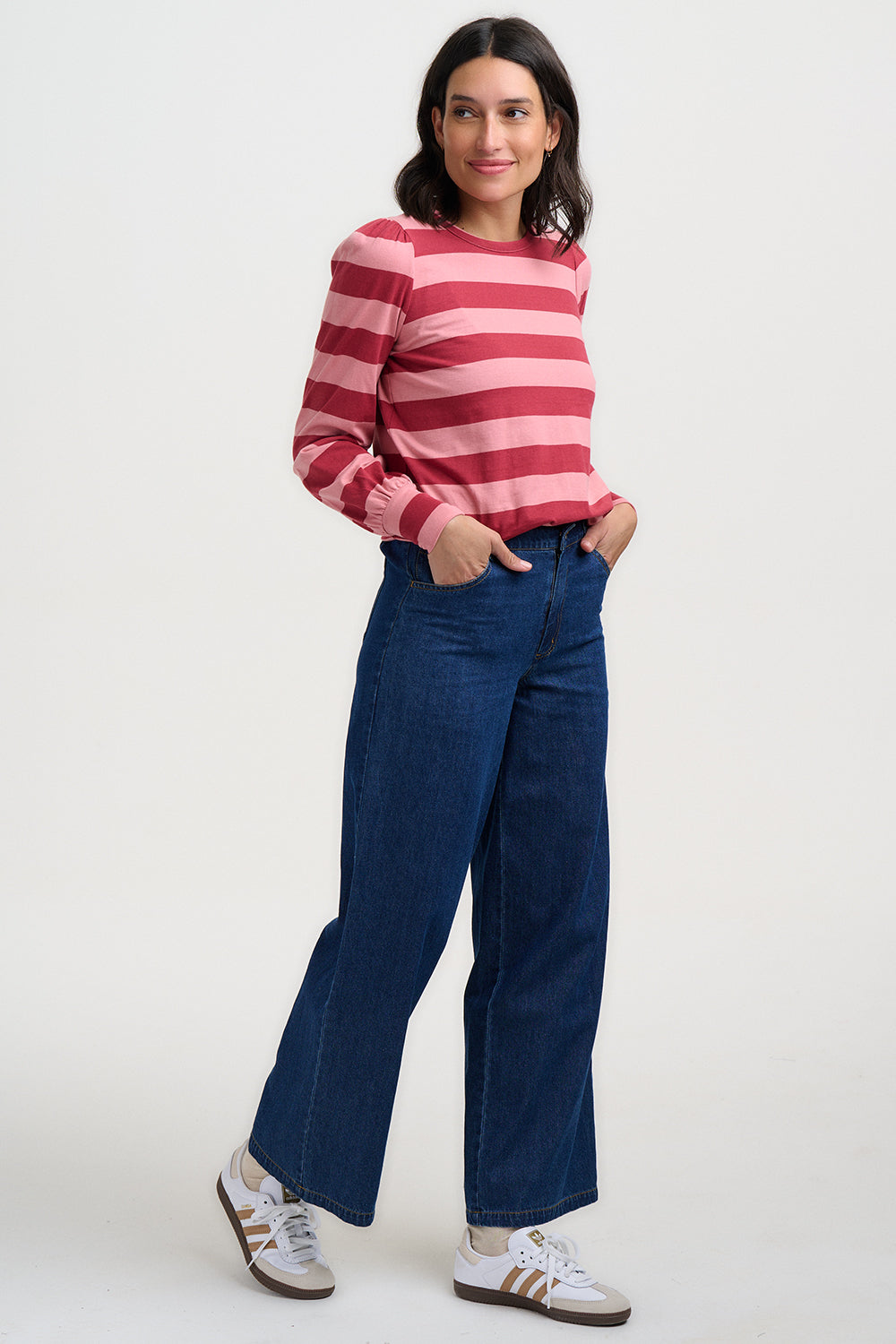 Woman wearing a red and pink striped sweater with blue jeans on a white background