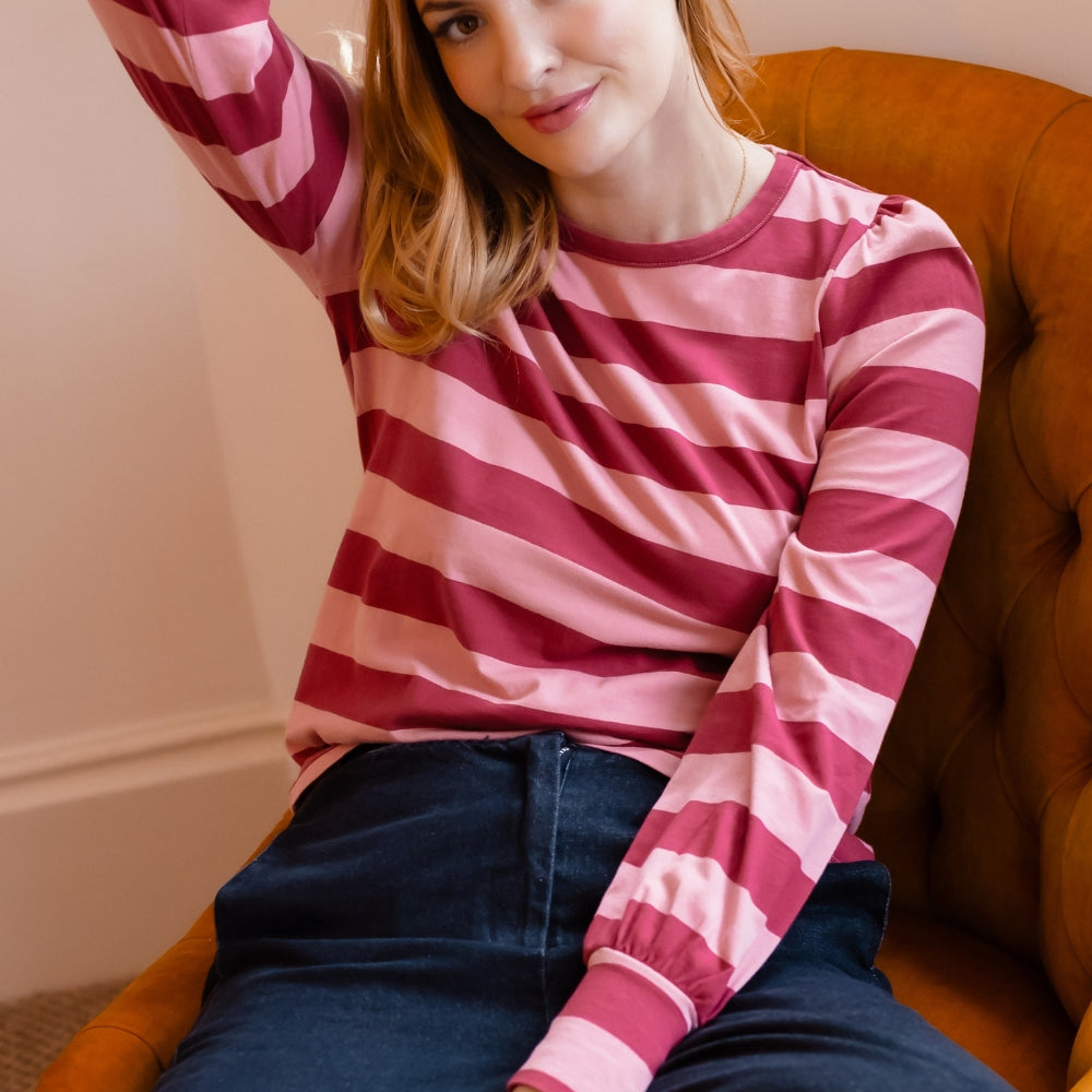 A woman wearing a pink and magenta striped long-sleeve top and dark blue jeans, sitting in an orange armchair.