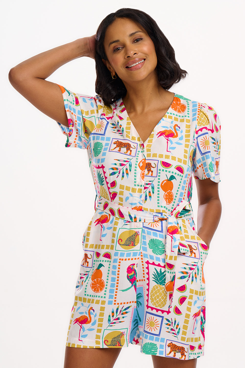 A model wearing an off-white playsuit with a colorful jungle tile print, featuring fluted sleeves and a deep V-neckline.