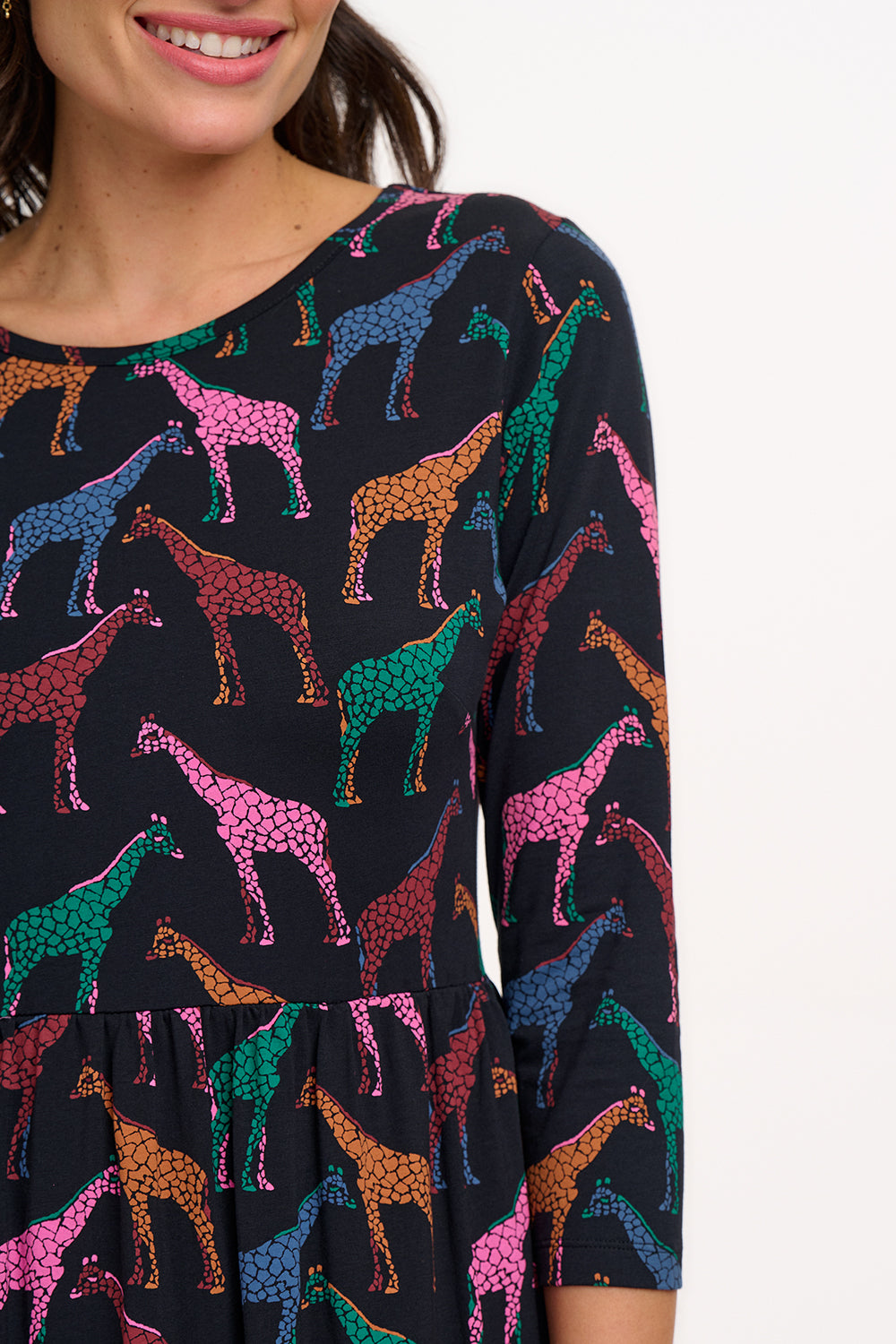 A model wearing a midi jersey dress with a gathered waist and 3/4 length sleeves. The dress has a black base with a colorful giraffe print.