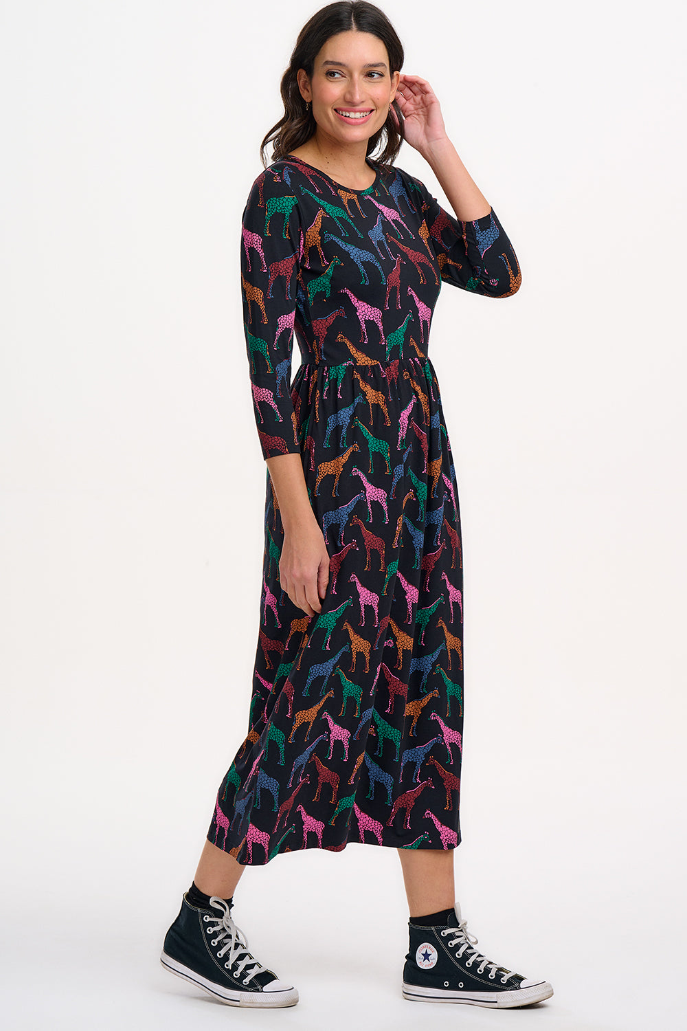 A model wearing a midi jersey dress with a gathered waist and 3/4 length sleeves. The dress has a black base with a colorful giraffe print.