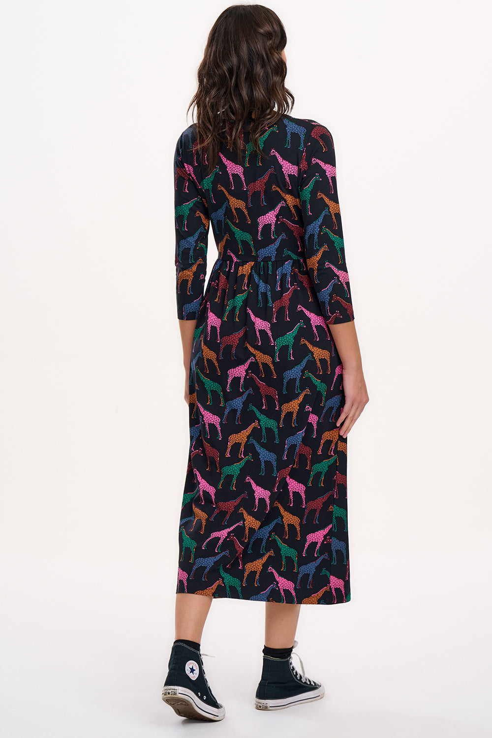 A model wearing a midi jersey dress with a gathered waist and 3/4 length sleeves. The dress has a black base with a colorful giraffe print.