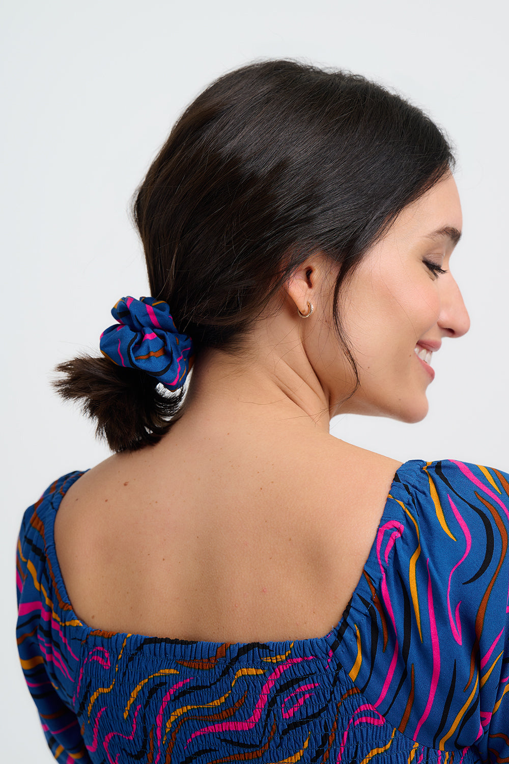 Woman with a blue hair tie in her ponytail wearing a colorful dress on a white background