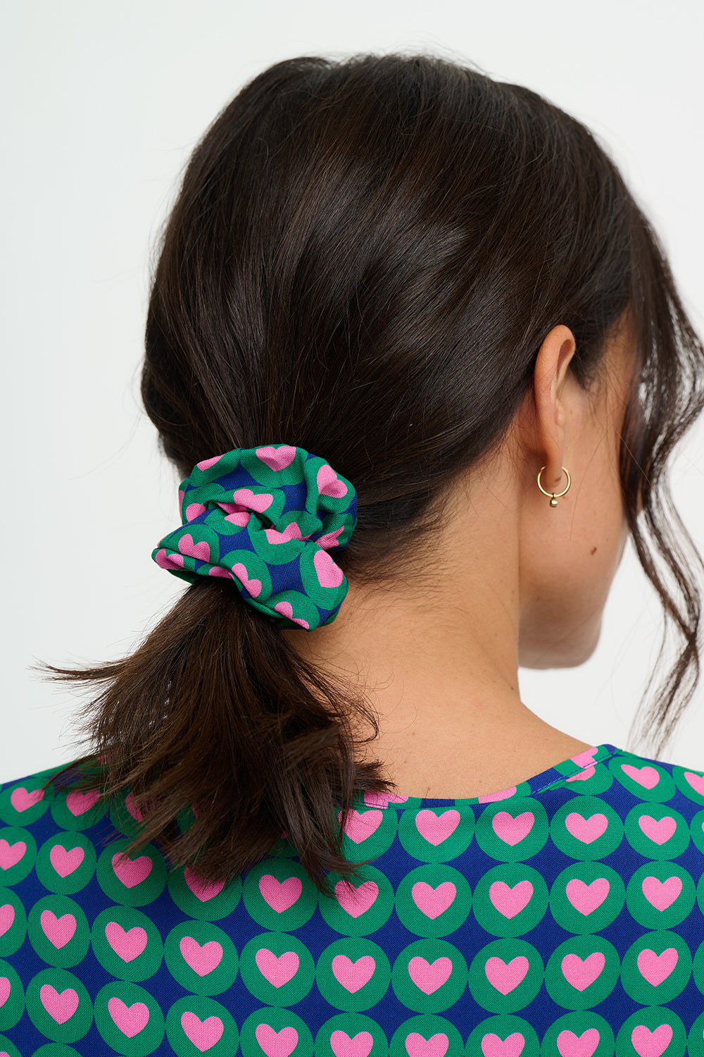 Person wearing a green scrunchie with pink hearts in their hair against a white background