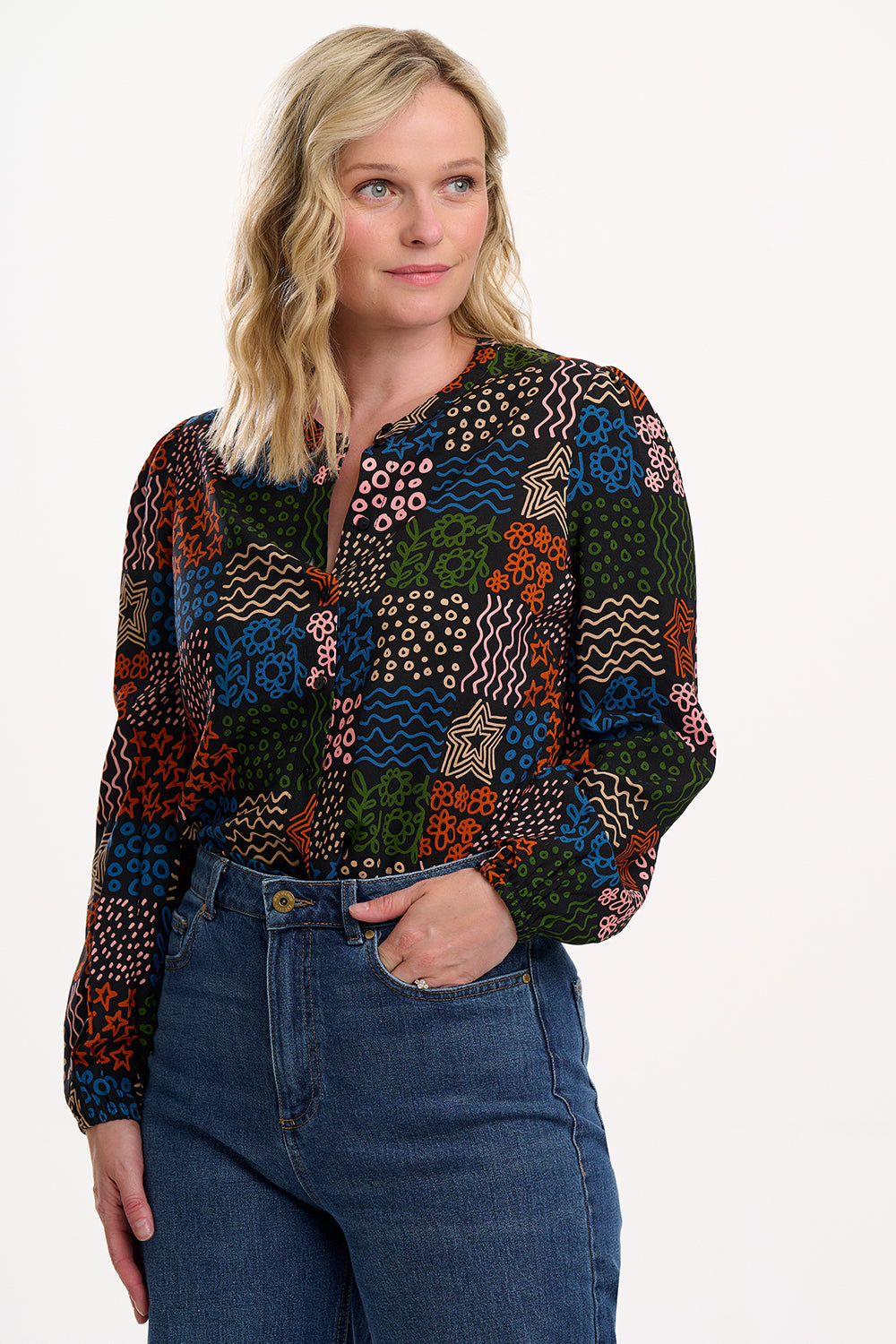 Woman wearing a colorful patterned shirt and blue jeans on a white background