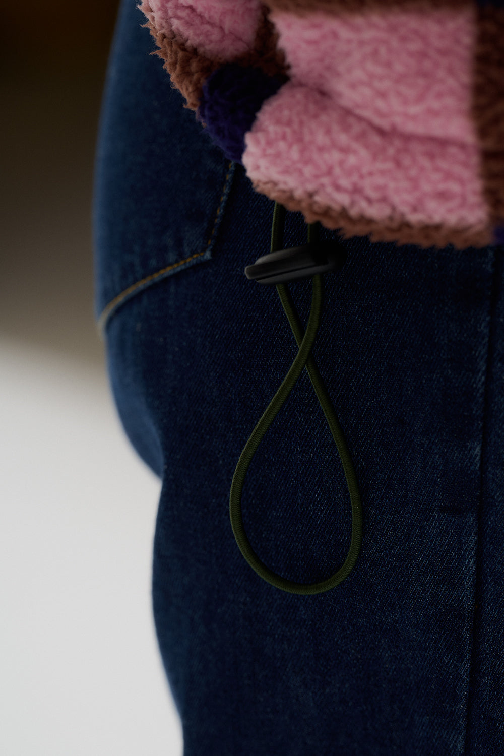 Close-up of a dark blue coat with a pink knitted sleeve and a green cord.