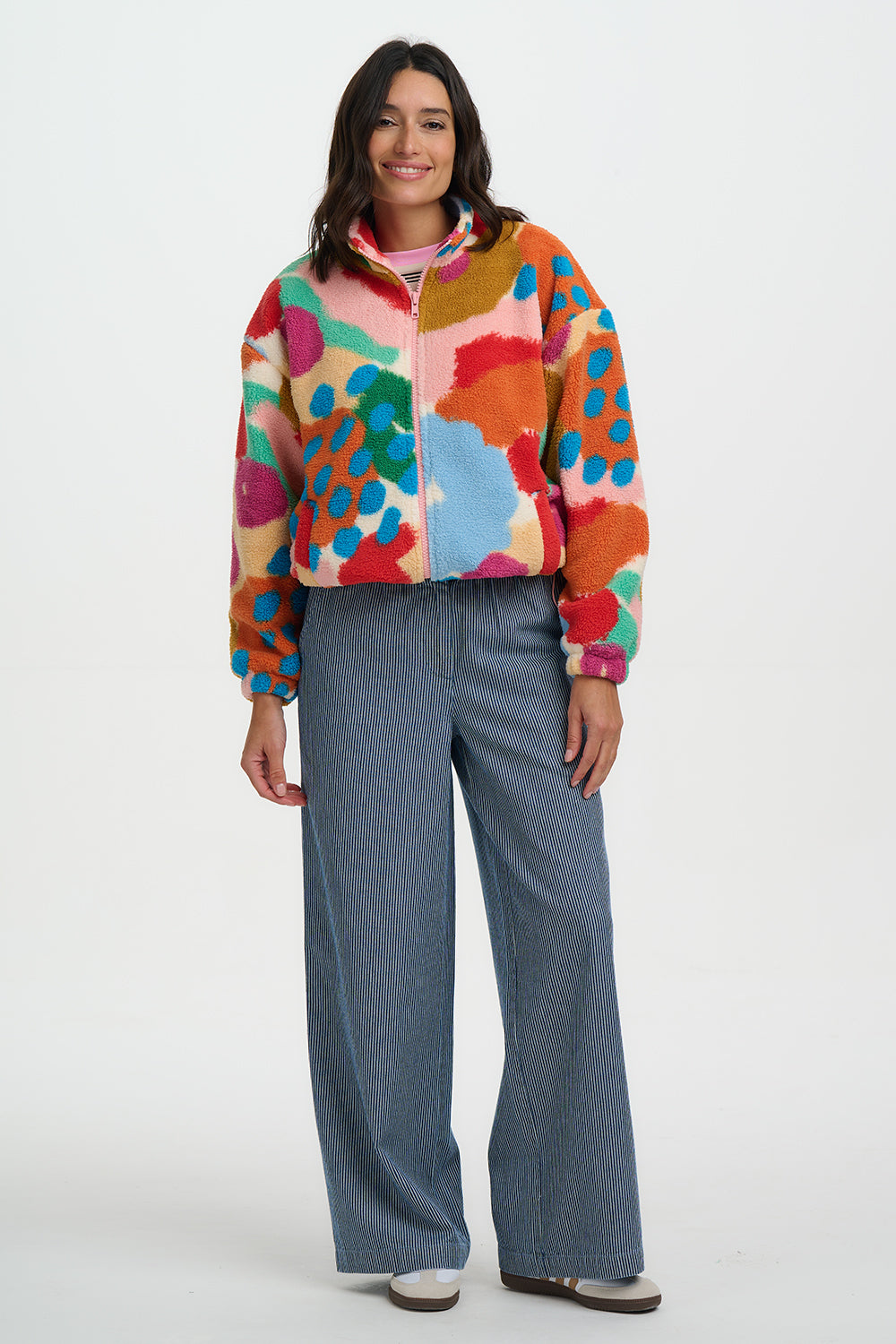 Person wearing a colorful jacket and blue pants on a white background