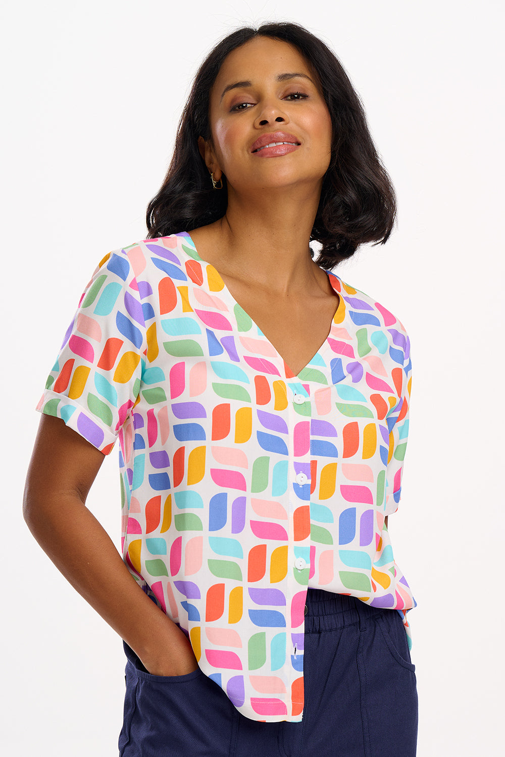 A woman wearing an off-white shirt with a colorful geometric print, short sleeves, and a V-neckline.