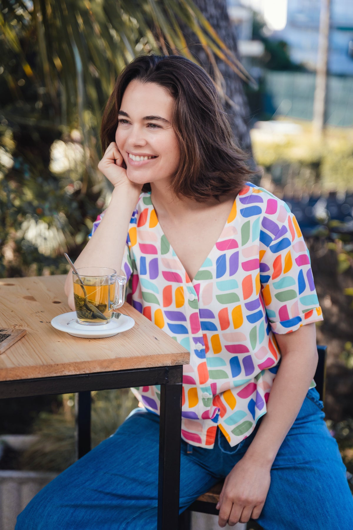 Woman sitting at an outdoor table with a colorful shirt and a drink.