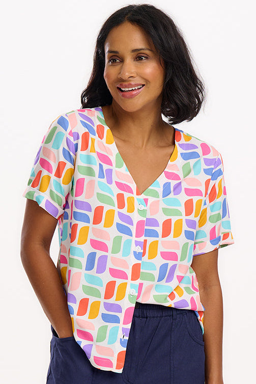 A woman wearing an off-white shirt with a colorful geometric print, short sleeves, and a V-neckline.