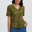 Woman wearing a green patterned blouse with blue pants on a white background