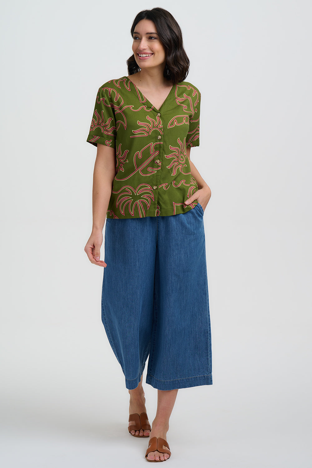 Woman wearing a green patterned top and blue pants on a white background