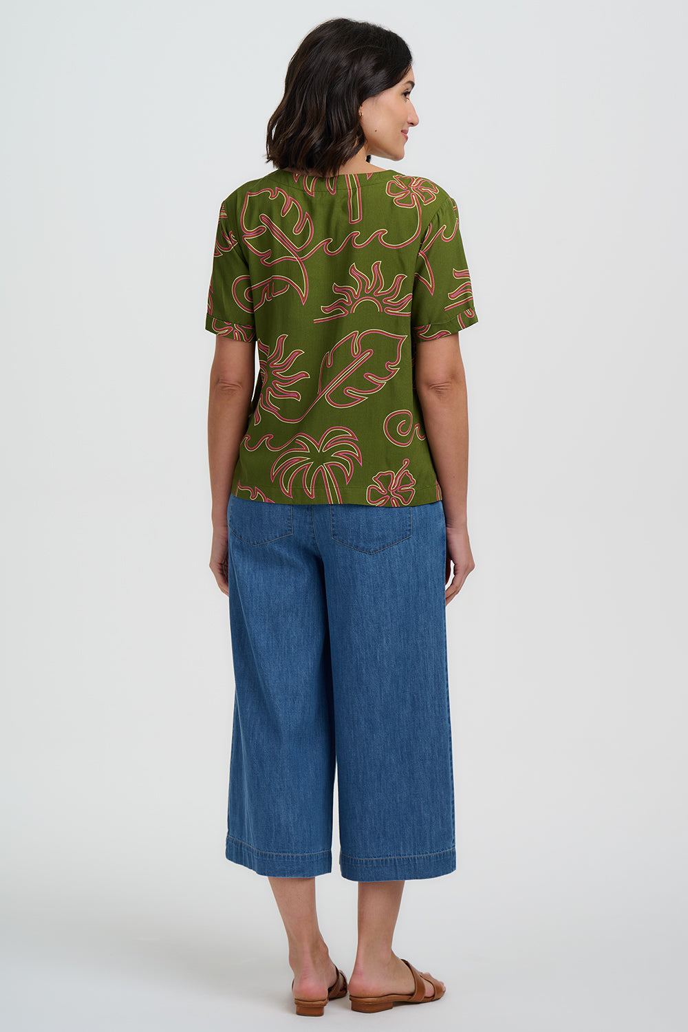 Woman wearing a green patterned top and blue pants on a white background