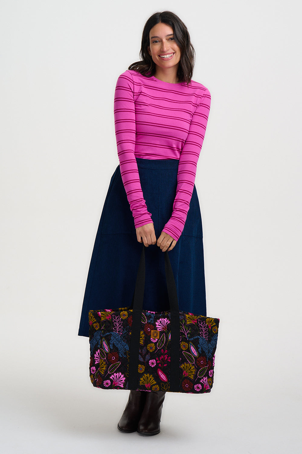 Woman wearing a pink striped sweater and navy skirt with floral pattern on a white background