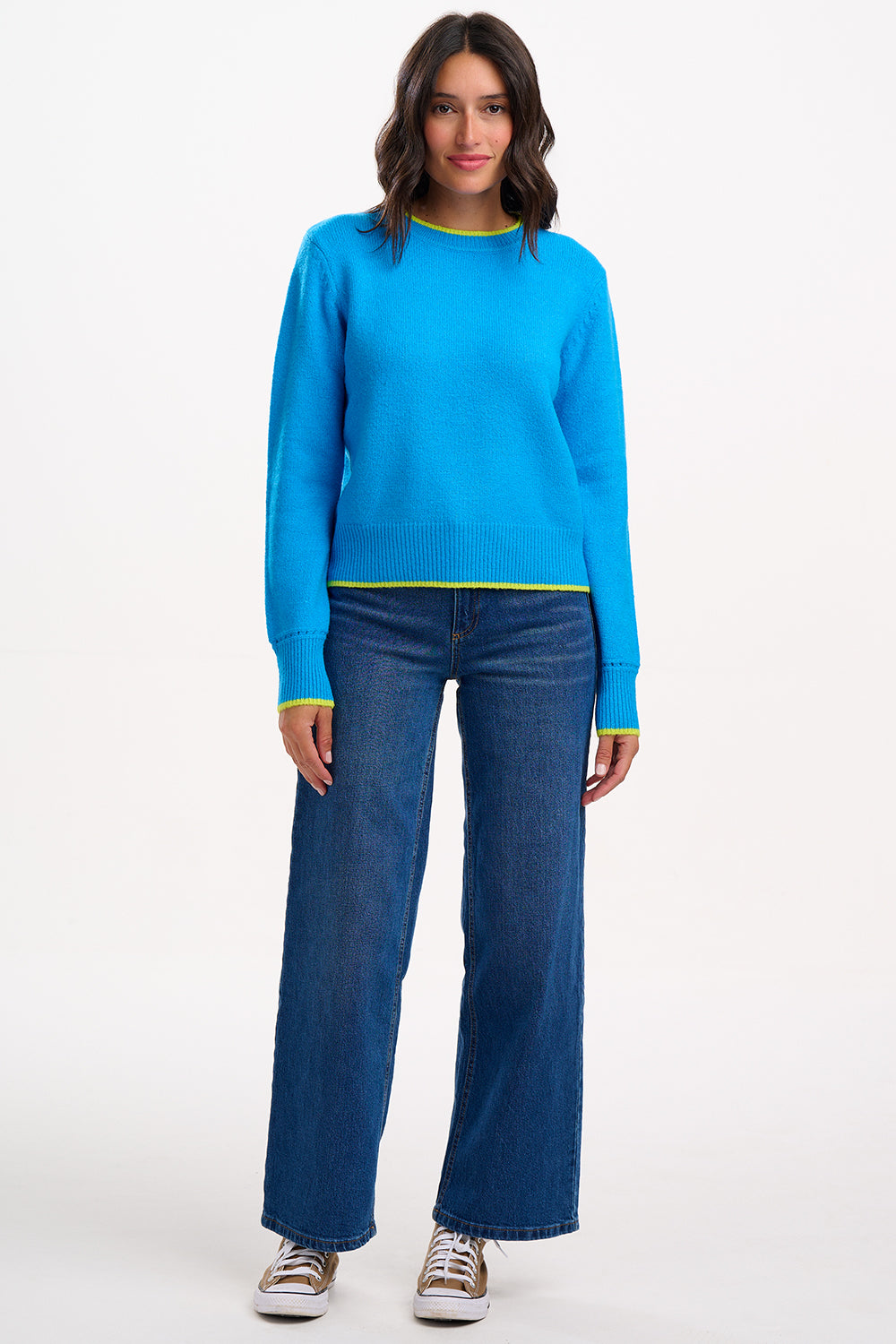 Sugarhill Brighton model wearing a blue sweater and jeans on a white background