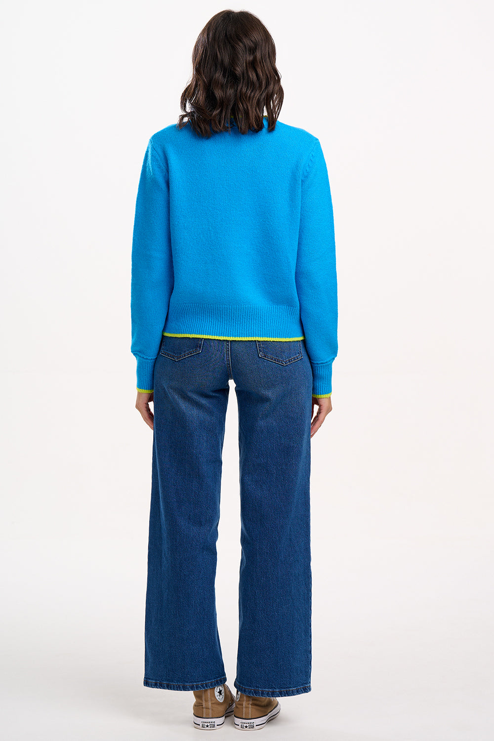 Sugarhill Brighton model wearing a blue sweater and jeans on a white background