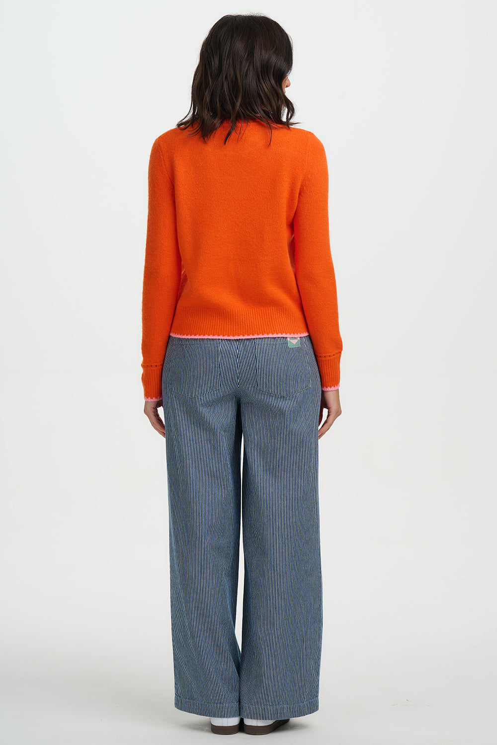 Person wearing an orange sweater and blue jeans on a white background