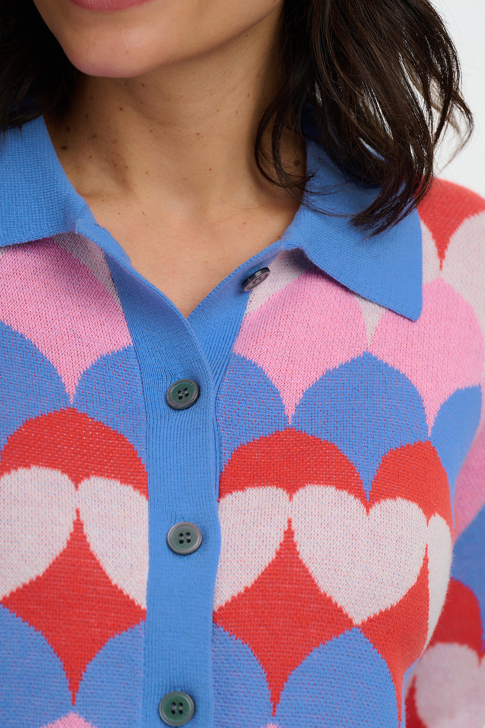 Person wearing a colorful patterned cardigan with pink, red, and blue hearts.