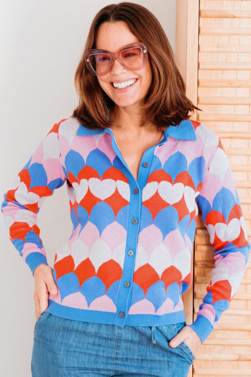 Woman wearing a colorful patterned cardigan with a white wall and wooden panel in the background