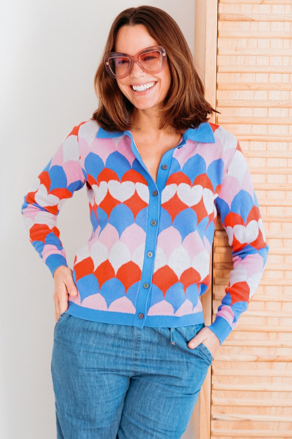 Woman wearing a colorful patterned cardigan with a white wall and wooden panel in the background