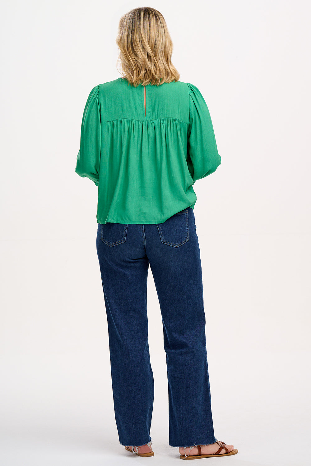 A woman wearing a green top with leopard floral embroidery, featuring a relaxed fit with blouson sleeves and gathered detailing, paired with jeans.