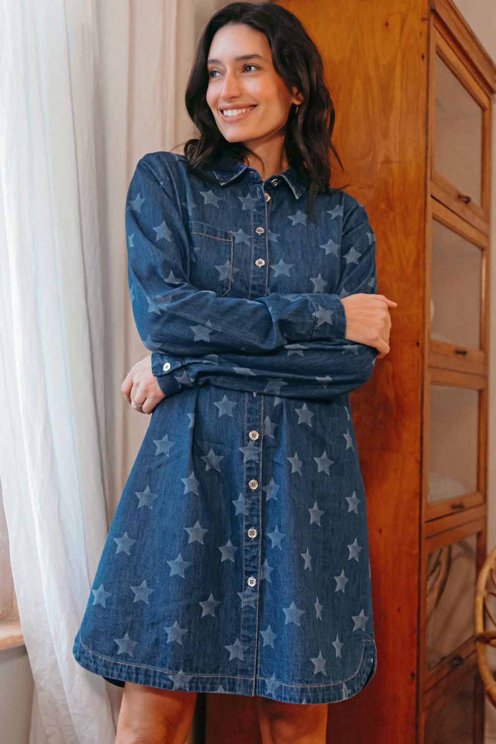 Woman wearing a blue denim dress with star patterns indoors.