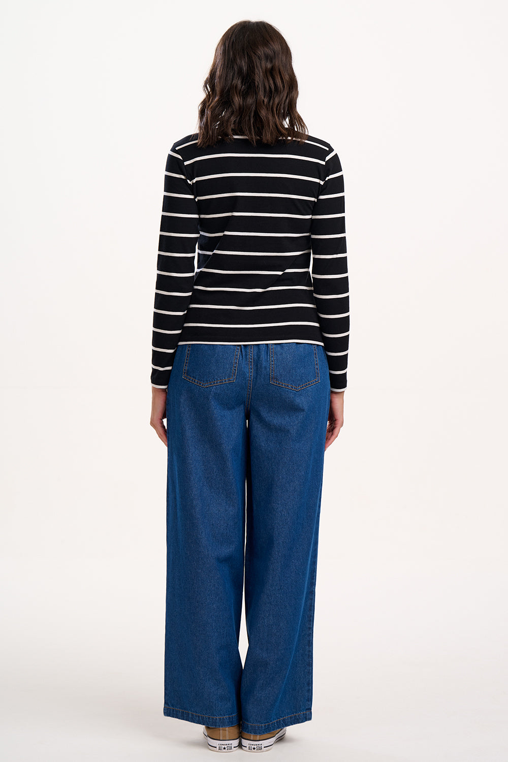 Sugarhill brigthon model wearing a black and white striped shirt and blue jeans on a white background