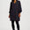 A woman modeling a long-sleeve V-neck mini dress with a dark base and a dense, small-scale multicolor geometric pattern, styled with black tights and black ankle boots against a light gray studio background.