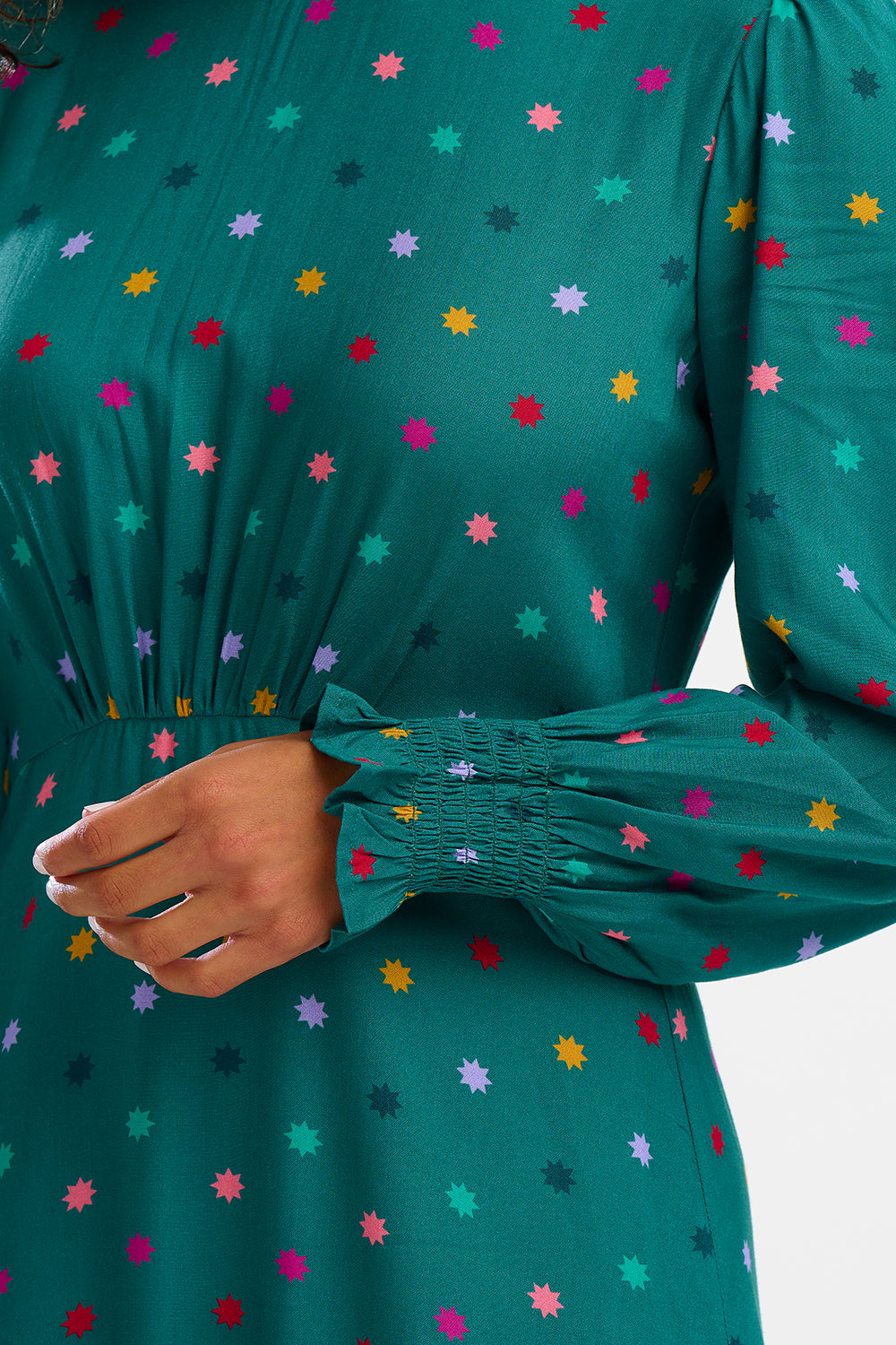 A woman standing and smiling, wearing a green maxi dress with a winter starburst pattern and long sleeves.
