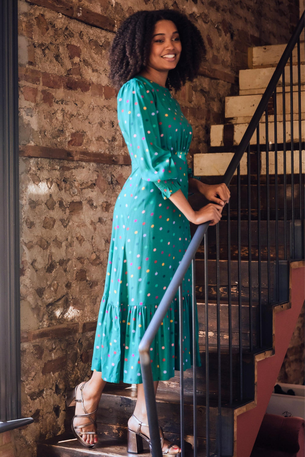 Woman in a green dress standing on a staircase with a brick wall background