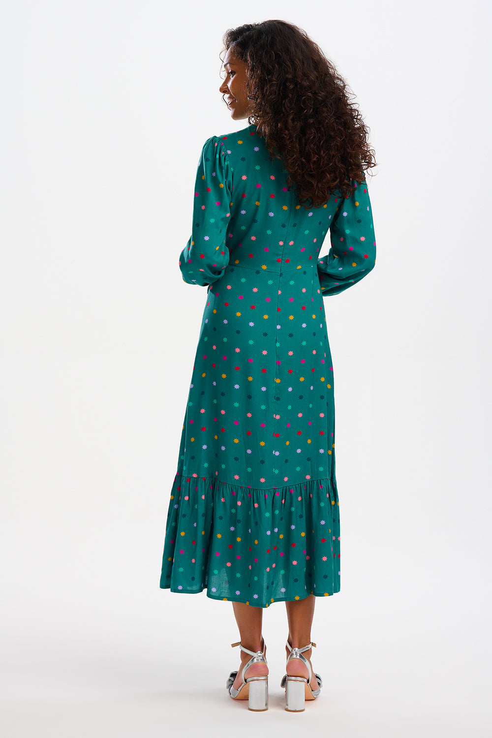 A woman standing and smiling, wearing a green maxi dress with a winter starburst pattern and long sleeves.