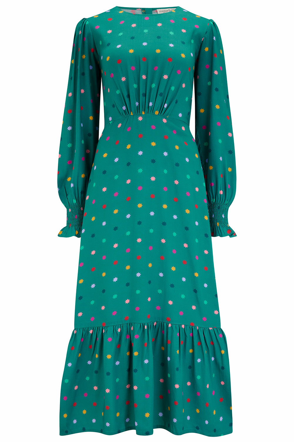 A woman standing and smiling, wearing a green maxi dress with a winter starburst pattern and long sleeves.