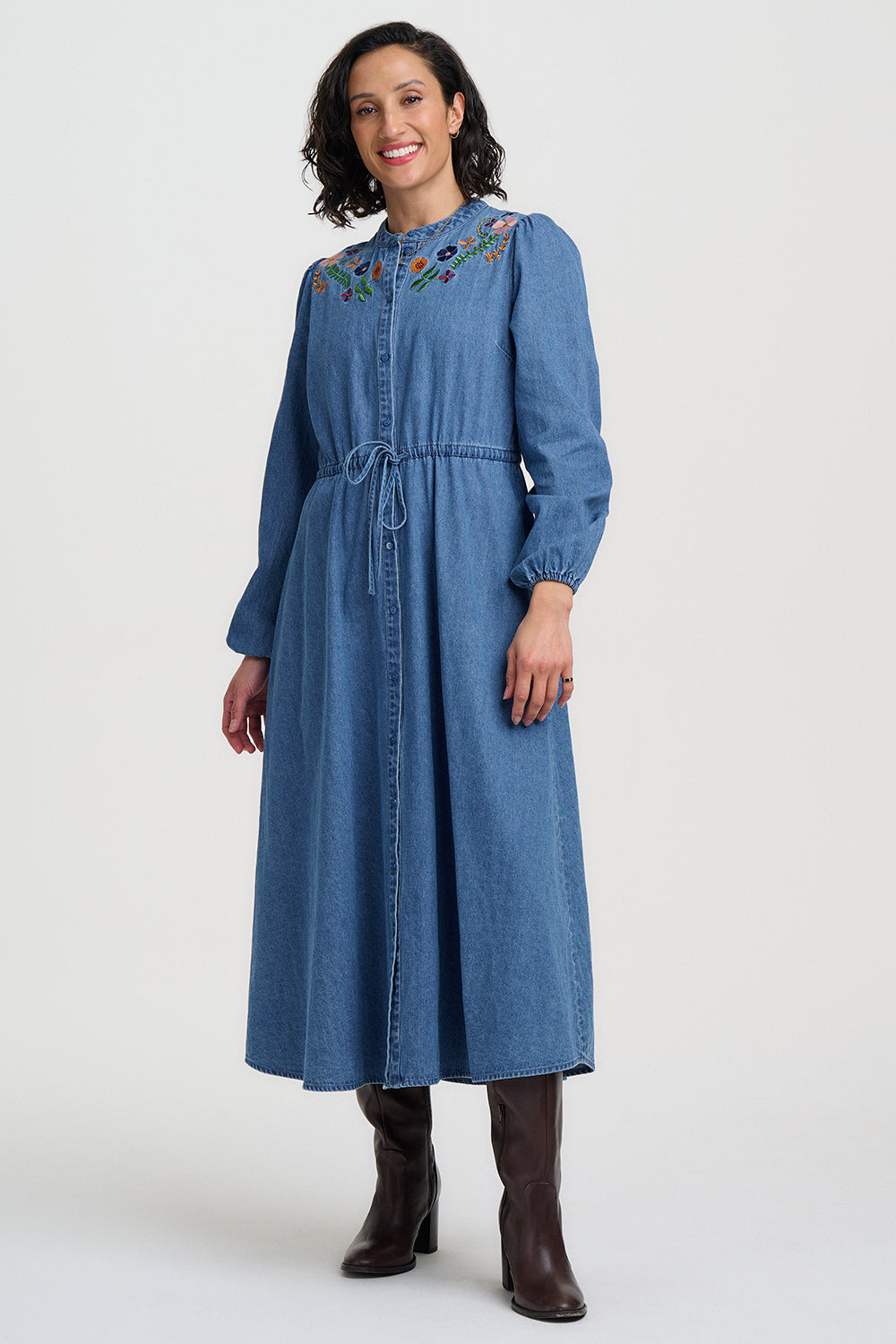 Woman wearing a blue denim dress with floral embroidery on a white background