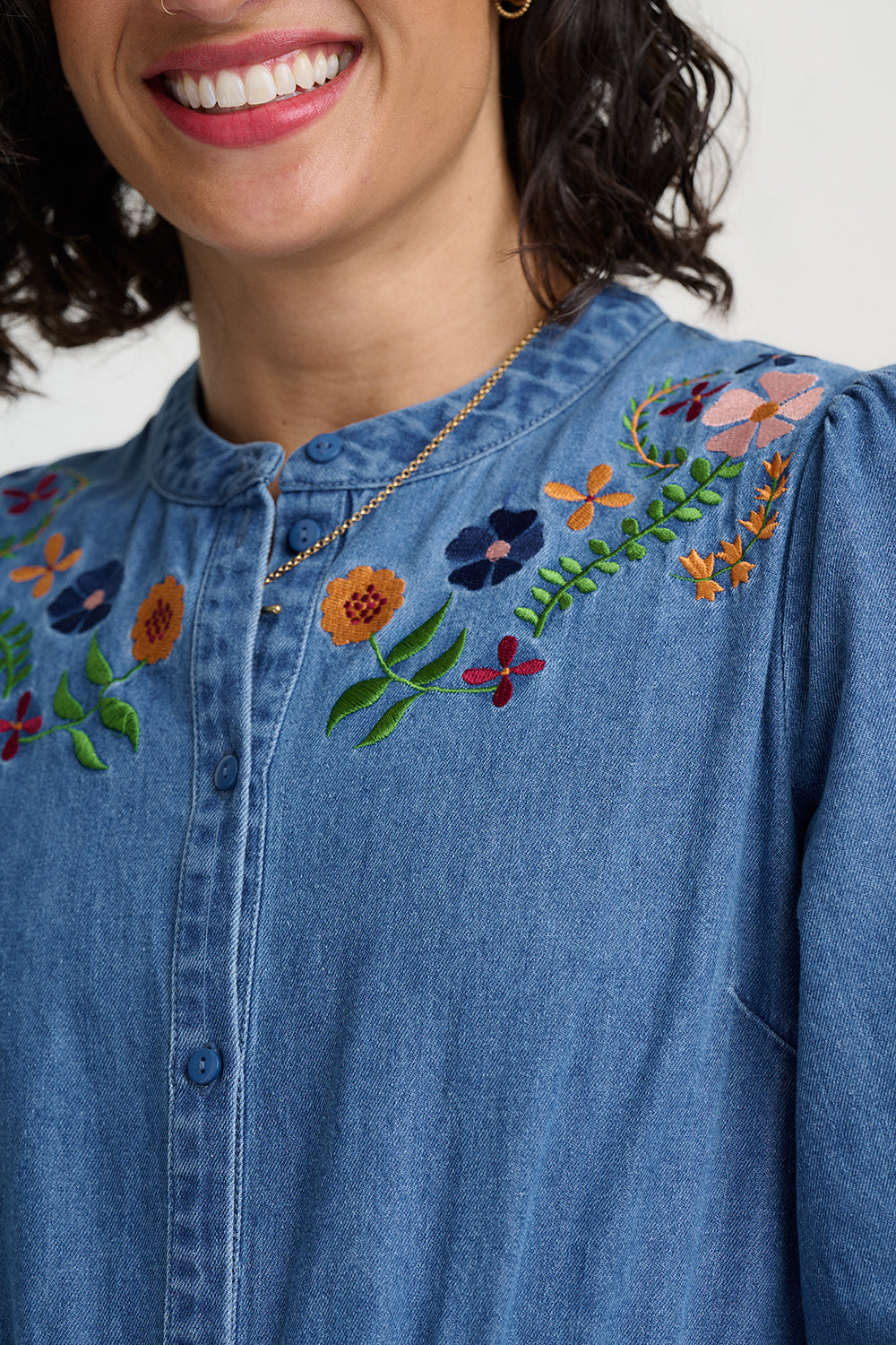 Close-up of a blue denim shirt with floral embroidery on a plain background