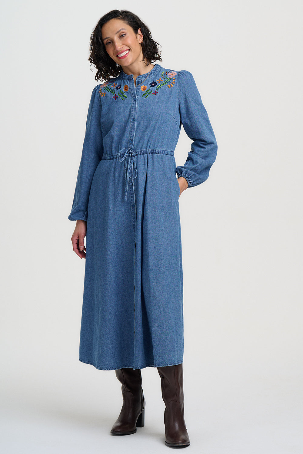 Woman wearing a blue denim dress with floral embroidery on a white background