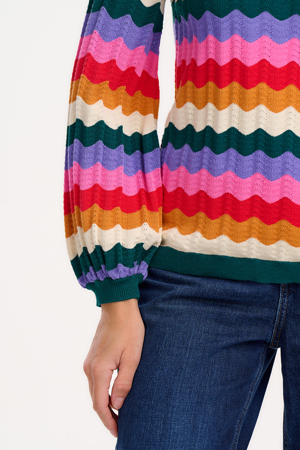 A woman wearing a multicolored striped jumper with a round neckline and long sleeves.