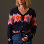 Woman wearing a dark blue cardigan with colorful geometric patterns and blue jeans against a brown background