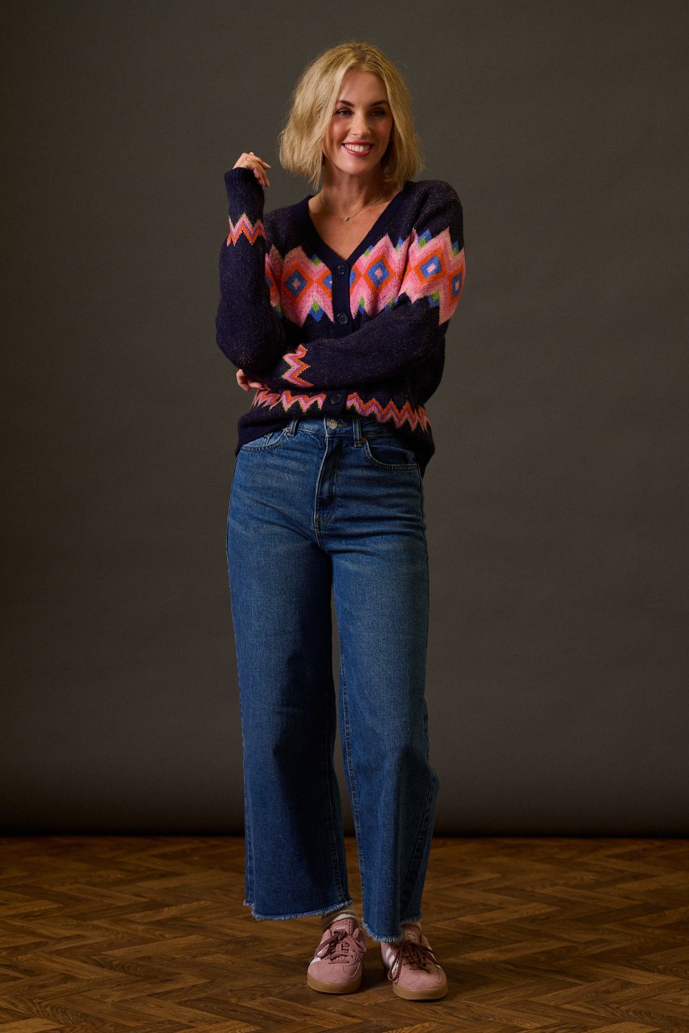 Woman wearing a patterned sweater and blue jeans against a plain background