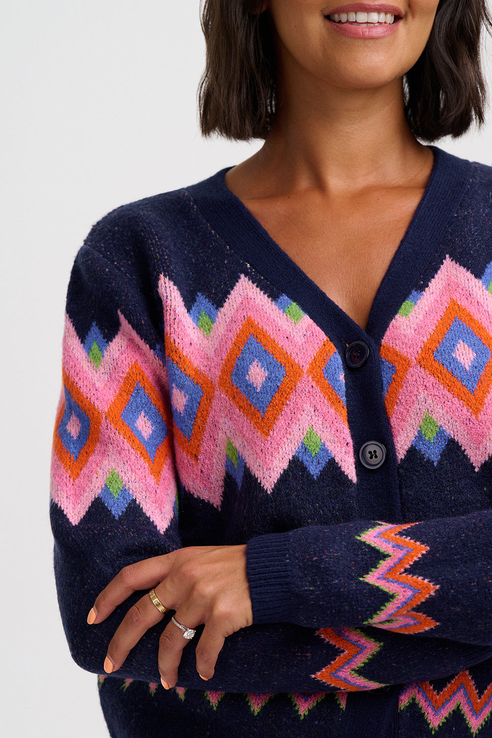 A close-up of a woman wearing a navy blue knit cardigan with a vibrant pink, orange, and blue geometric diamond pattern across the chest and sleeves.