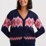 A woman wearing a navy blue button-up cardigan with a colorful geometric pattern in pink, orange, and blue, paired with dark blue jeans, against a light gray studio background.