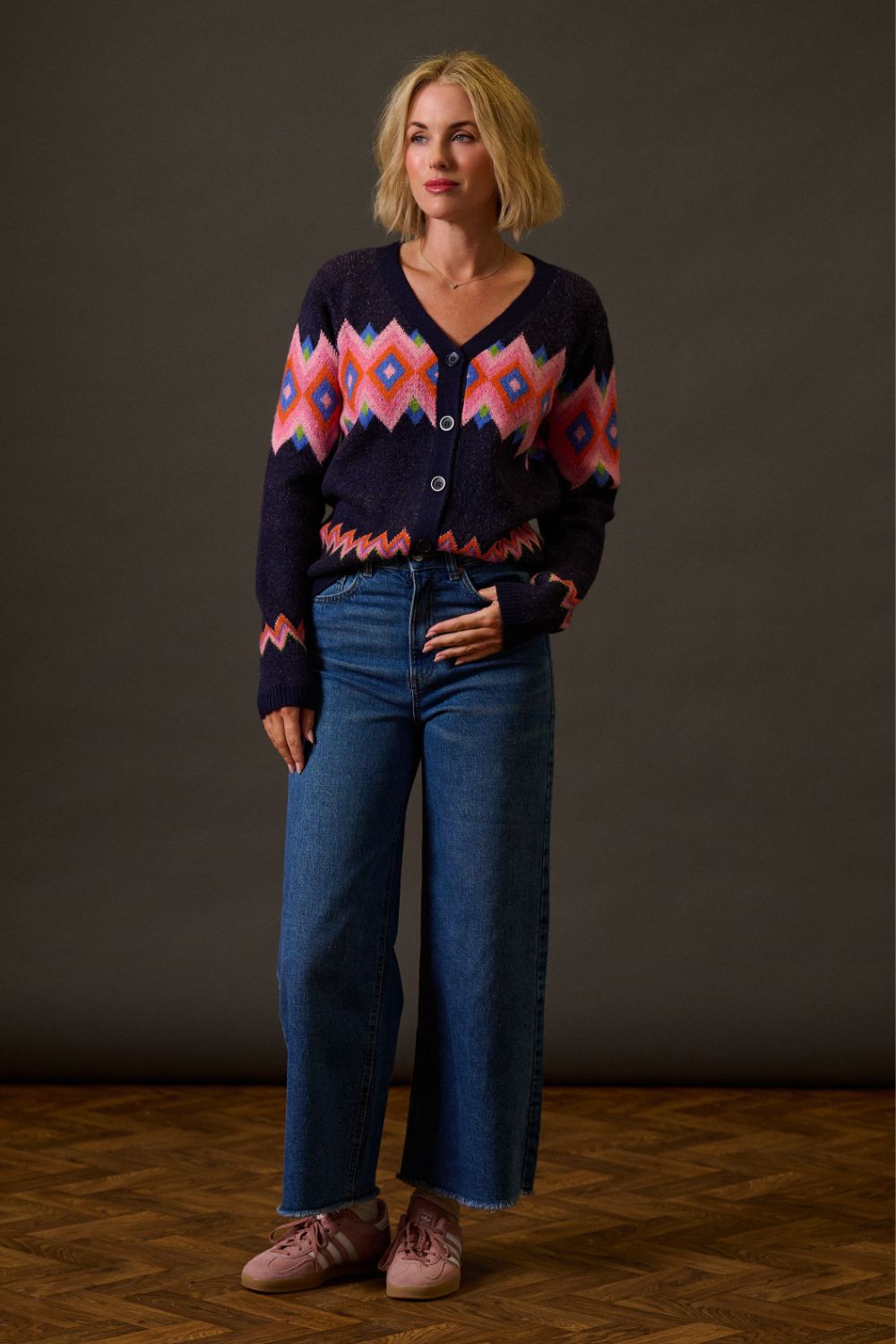 Woman wearing a patterned sweater and blue jeans against a plain background