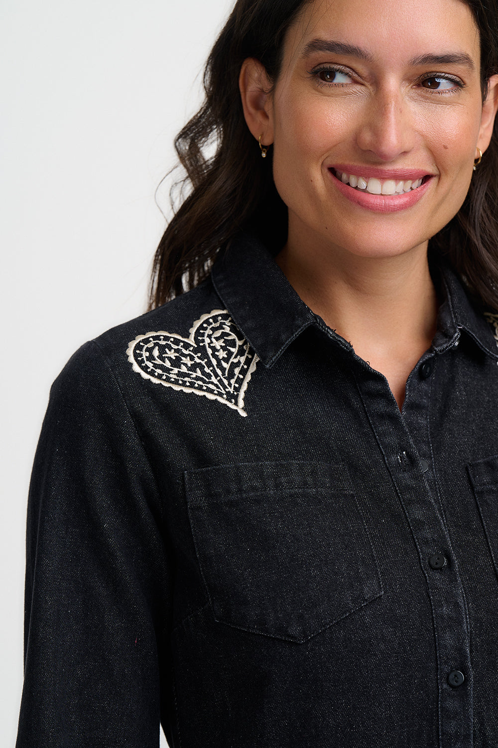 Woman wearing a black shirt with a decorative heart brooch on a white background