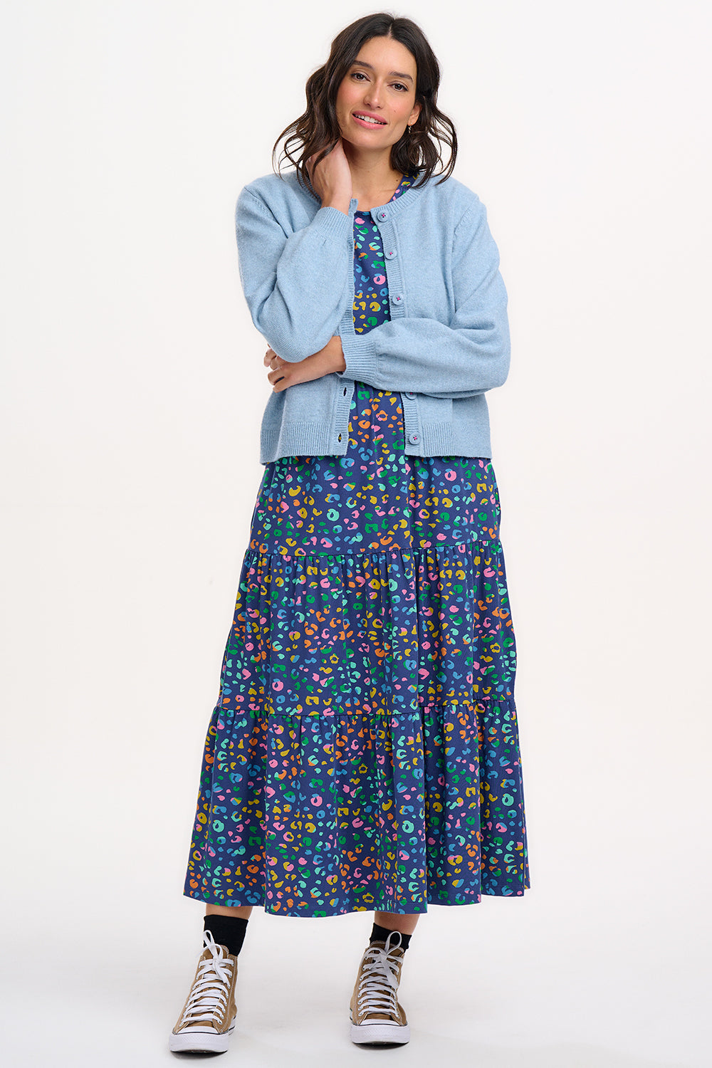 A woman wearing a sky blue Jamie Cardigan with ribbed round neck, buttoned front, and blouson sleeve. The cardigan features small matching sky blue buttons with accent hot pink stitching.